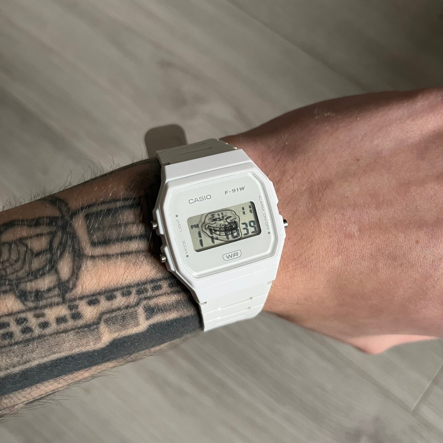 Custom Casio F-91W White digital watch featuring a Trollface meme filter screen. Slim 8.5 mm profile, lightweight 21 g build and flexible bio-based resin band ensure lasting comfort. Includes alarm, stopwatch, and microlight function for everyday functionality.