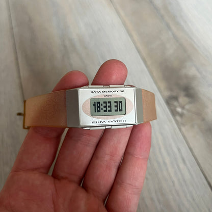 Casio FS-06 Data Memory-30 “Film Watch” is a vintage mid-1980s digital timepiece featuring a rectangular silver case with salmon accents. It includes a semi-transparent orange strap with a floral pattern and a strong blue backlight display. The watch offers multiple functions such as world time, dual alarms, chronograph, and memo/data memory mode. It is made in Malaysia and features tactile buttons, illuminated display, and a signed case back.