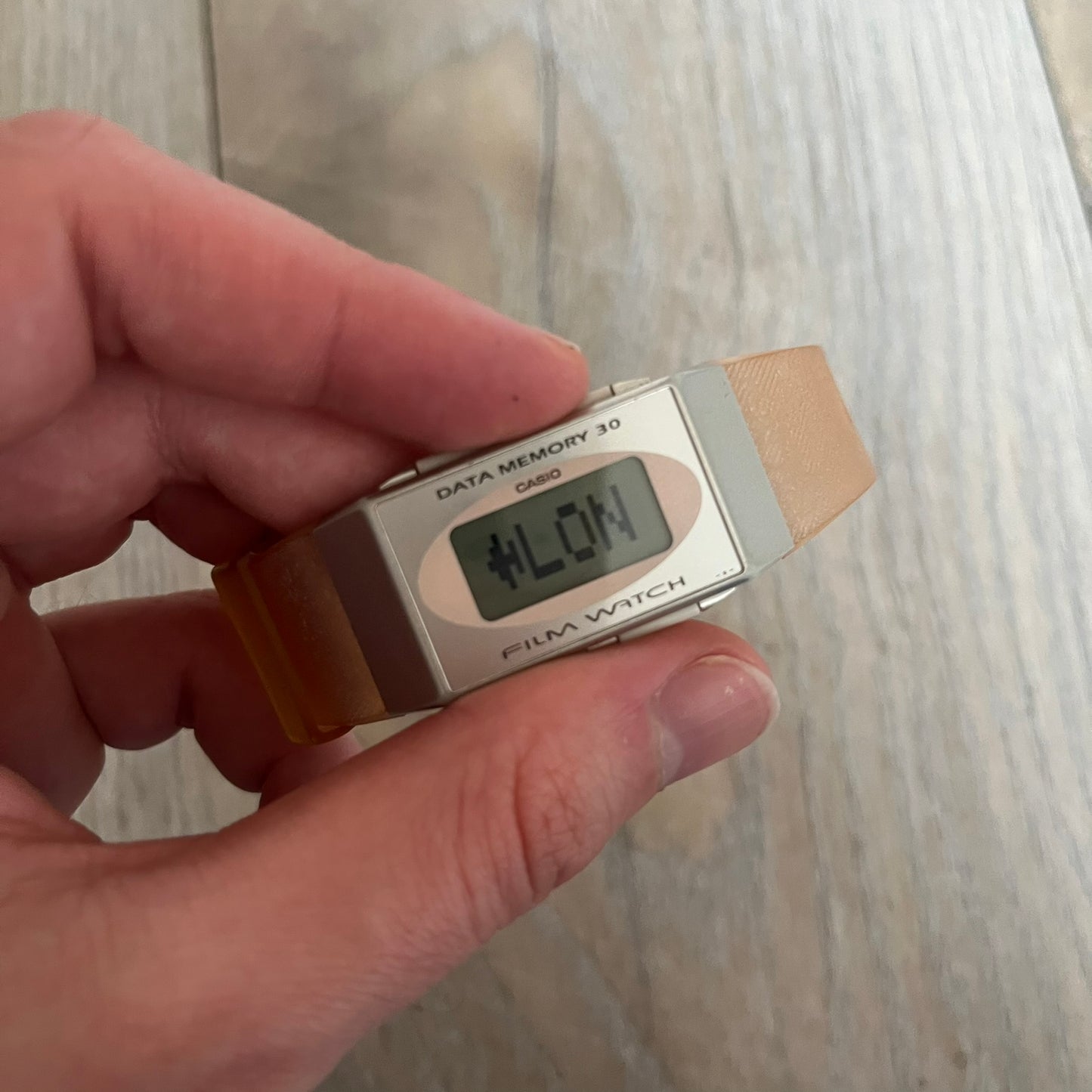 Casio FS-06 Data Memory-30 “Film Watch” is a vintage mid-1980s digital timepiece featuring a rectangular silver case with salmon accents. It includes a semi-transparent orange strap with a floral pattern and a strong blue backlight display. The watch offers multiple functions such as world time, dual alarms, chronograph, and memo/data memory mode. It is made in Malaysia and features tactile buttons, illuminated display, and a signed case back.