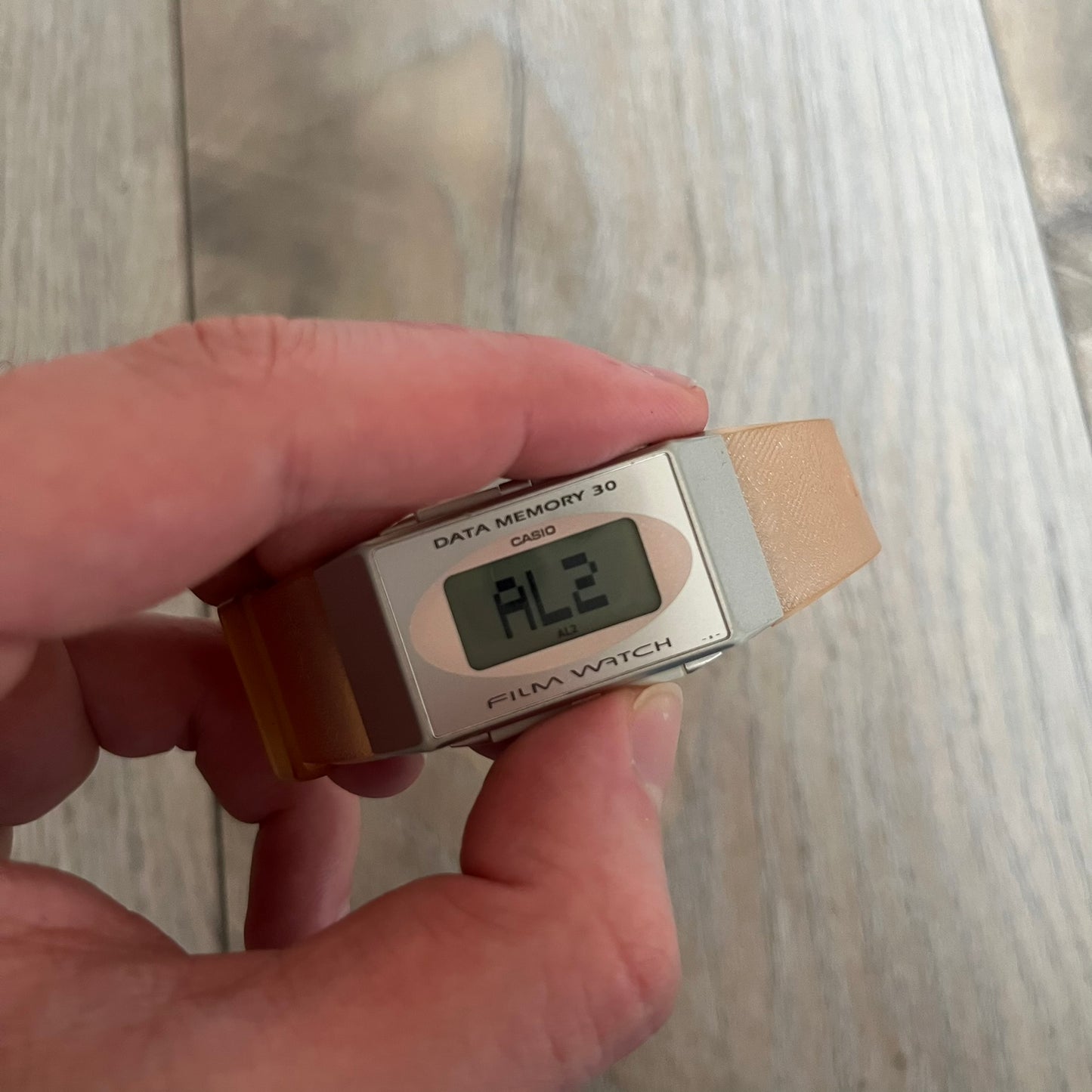 Casio FS-06 Data Memory-30 “Film Watch” is a vintage mid-1980s digital timepiece featuring a rectangular silver case with salmon accents. It includes a semi-transparent orange strap with a floral pattern and a strong blue backlight display. The watch offers multiple functions such as world time, dual alarms, chronograph, and memo/data memory mode. It is made in Malaysia and features tactile buttons, illuminated display, and a signed case back.