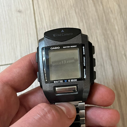 Casio Wrist Camera 2220 WQV-1 Digital Watch from the 2000s, made in Japan. Features a built-in camera module at the top, with six function buttons for photo capture, IR communication, alarm, timer, stopwatch, and gallery viewing. Monochrome photo output in shades of black, white, and gray; fitted with a non-original bracelet.
