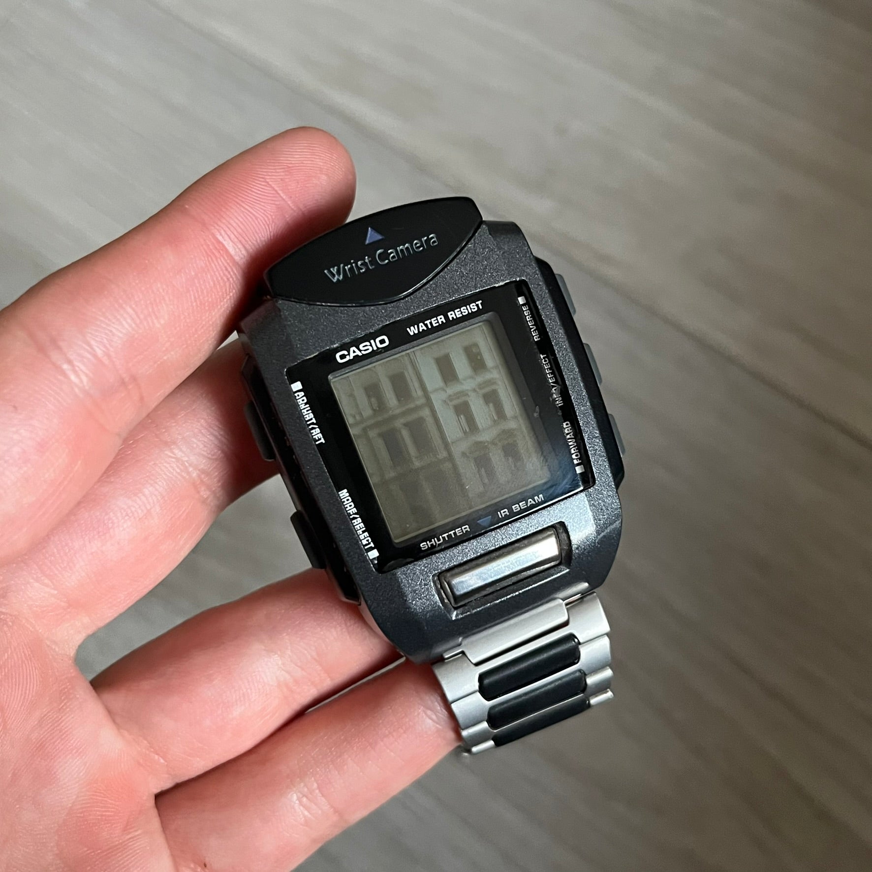 Casio Wrist Camera 2220 WQV-1 Digital Watch from the 2000s, made in Japan. Features a built-in camera module at the top, with six function buttons for photo capture, IR communication, alarm, timer, stopwatch, and gallery viewing. Monochrome photo output in shades of black, white, and gray; fitted with a non-original bracelet.