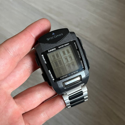 Casio Wrist Camera 2220 WQV-1 Digital Watch from the 2000s, made in Japan. Features a built-in camera module at the top, with six function buttons for photo capture, IR communication, alarm, timer, stopwatch, and gallery viewing. Monochrome photo output in shades of black, white, and gray; fitted with a non-original bracelet.