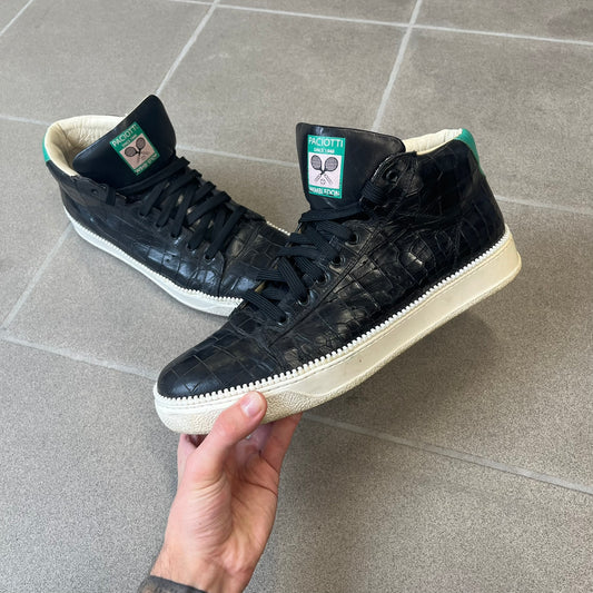 Cesare Paciotti Wimbledon Cocco Lux Black Sneakers (CPM5121) are made in Italy from black crocodile-embossed leather, with a Paciotti Wimbledon tag showing two rackets on the tongue and a second logo on the heel. The white rubber sole has a textured zipper-teeth detail running around its edge. They come with the original box, which shows wear.
