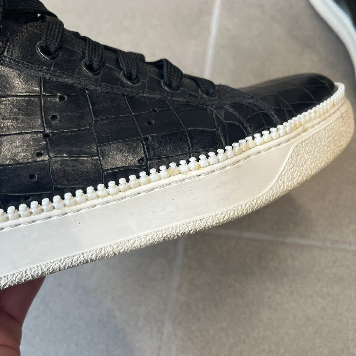 Cesare Paciotti Wimbledon Cocco Lux Black Sneakers (CPM5121) are made in Italy from black crocodile-embossed leather, with a Paciotti Wimbledon tag showing two rackets on the tongue and a second logo on the heel. The white rubber sole has a textured zipper-teeth detail running around its edge. They come with the original box, which shows wear.