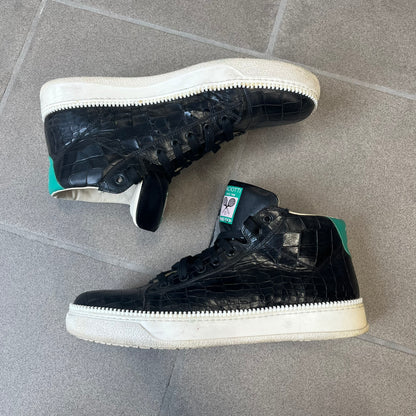 Cesare Paciotti Wimbledon Cocco Lux Black Sneakers (CPM5121) are made in Italy from black crocodile-embossed leather, with a Paciotti Wimbledon tag showing two rackets on the tongue and a second logo on the heel. The white rubber sole has a textured zipper-teeth detail running around its edge. They come with the original box, which shows wear.