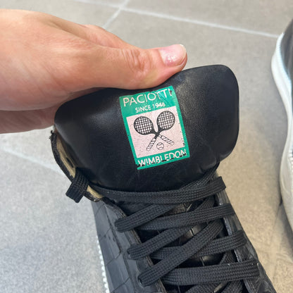 Cesare Paciotti Wimbledon Cocco Lux Black Sneakers (CPM5121) are made in Italy from black crocodile-embossed leather, with a Paciotti Wimbledon tag showing two rackets on the tongue and a second logo on the heel. The white rubber sole has a textured zipper-teeth detail running around its edge. They come with the original box, which shows wear.