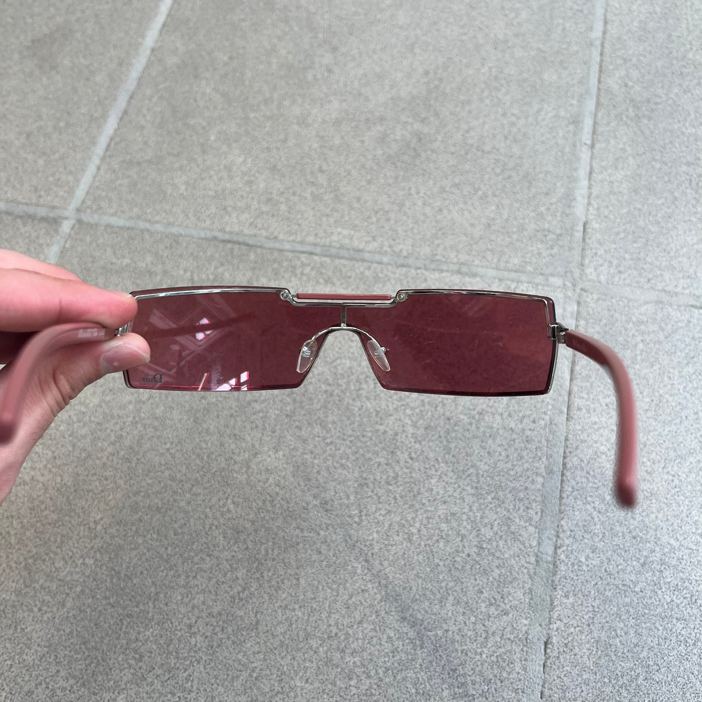 Christian Dior Viktim 2 Pink Sunglasses are an early 2000's eyewear piece from the Safilo era, featuring a futuristic rimless shield silhouette with a sleek wraparound lens design. The sunglasses have a pink/rose tinted lens with subtle Dior logo details at the bottom and minimalist framing. Made in Austria, they come complete with a silver Dior case.