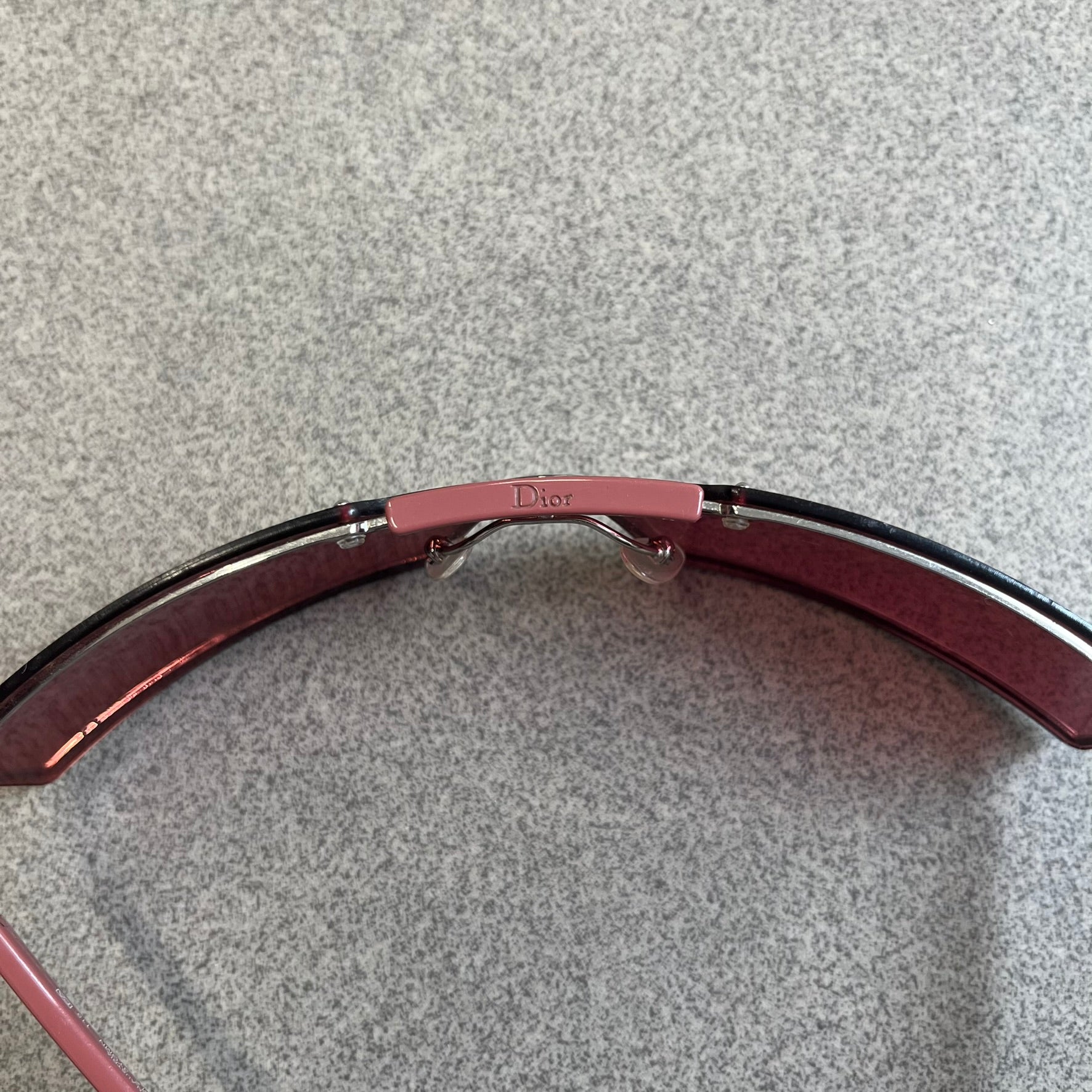 Christian Dior Viktim 2 Pink Sunglasses are an early 2000's eyewear piece from the Safilo era, featuring a futuristic rimless shield silhouette with a sleek wraparound lens design. The sunglasses have a pink/rose tinted lens with subtle Dior logo details at the bottom and minimalist framing. Made in Austria, they come complete with a silver Dior case.