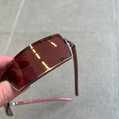 Christian Dior Viktim 2 Pink Sunglasses are an early 2000's eyewear piece from the Safilo era, featuring a futuristic rimless shield silhouette with a sleek wraparound lens design. The sunglasses have a pink/rose tinted lens with subtle Dior logo details at the bottom and minimalist framing. Made in Austria, they come complete with a silver Dior case.