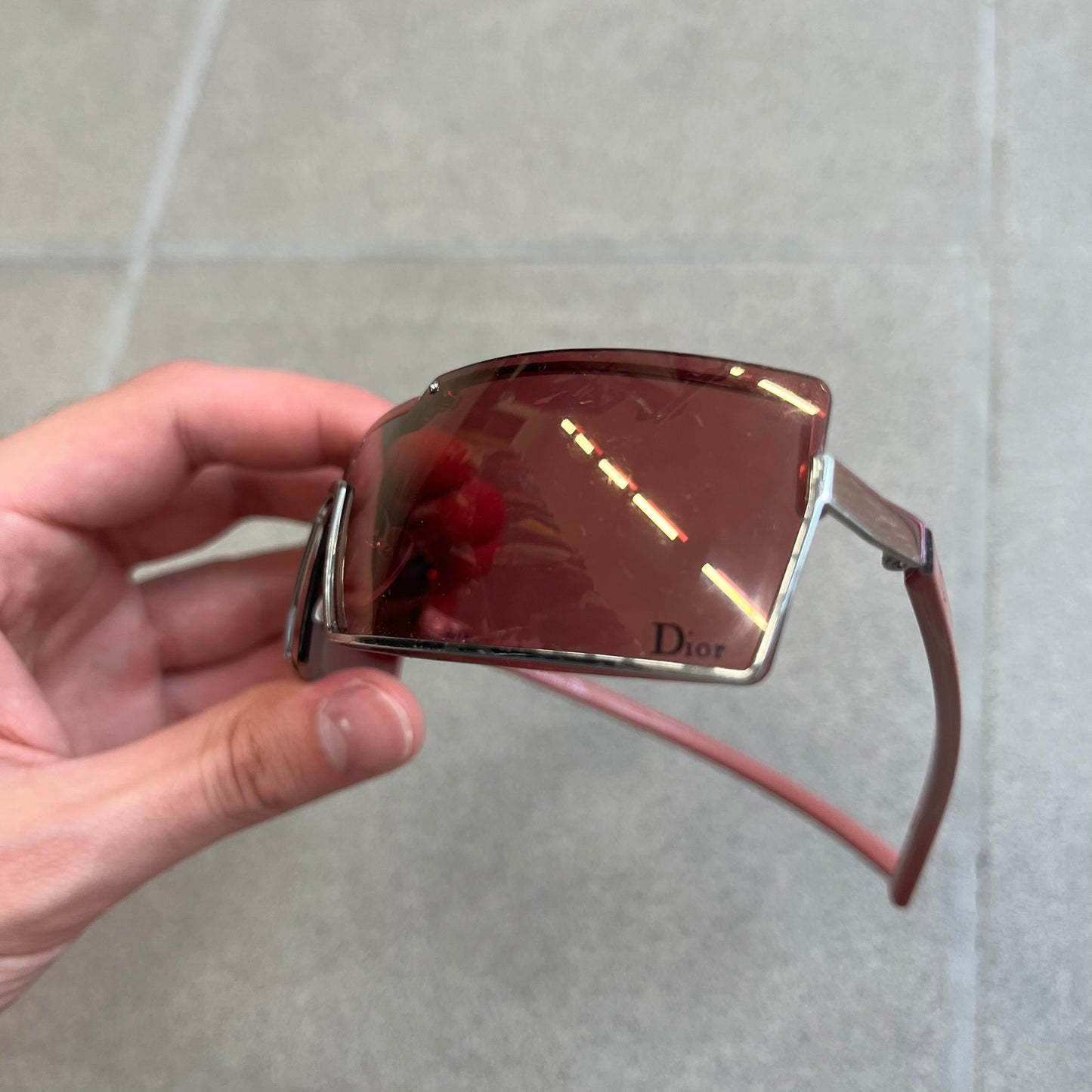 Christian Dior Viktim 2 Pink Sunglasses are an early 2000's eyewear piece from the Safilo era, featuring a futuristic rimless shield silhouette with a sleek wraparound lens design. The sunglasses have a pink/rose tinted lens with subtle Dior logo details at the bottom and minimalist framing. Made in Austria, they come complete with a silver Dior case.