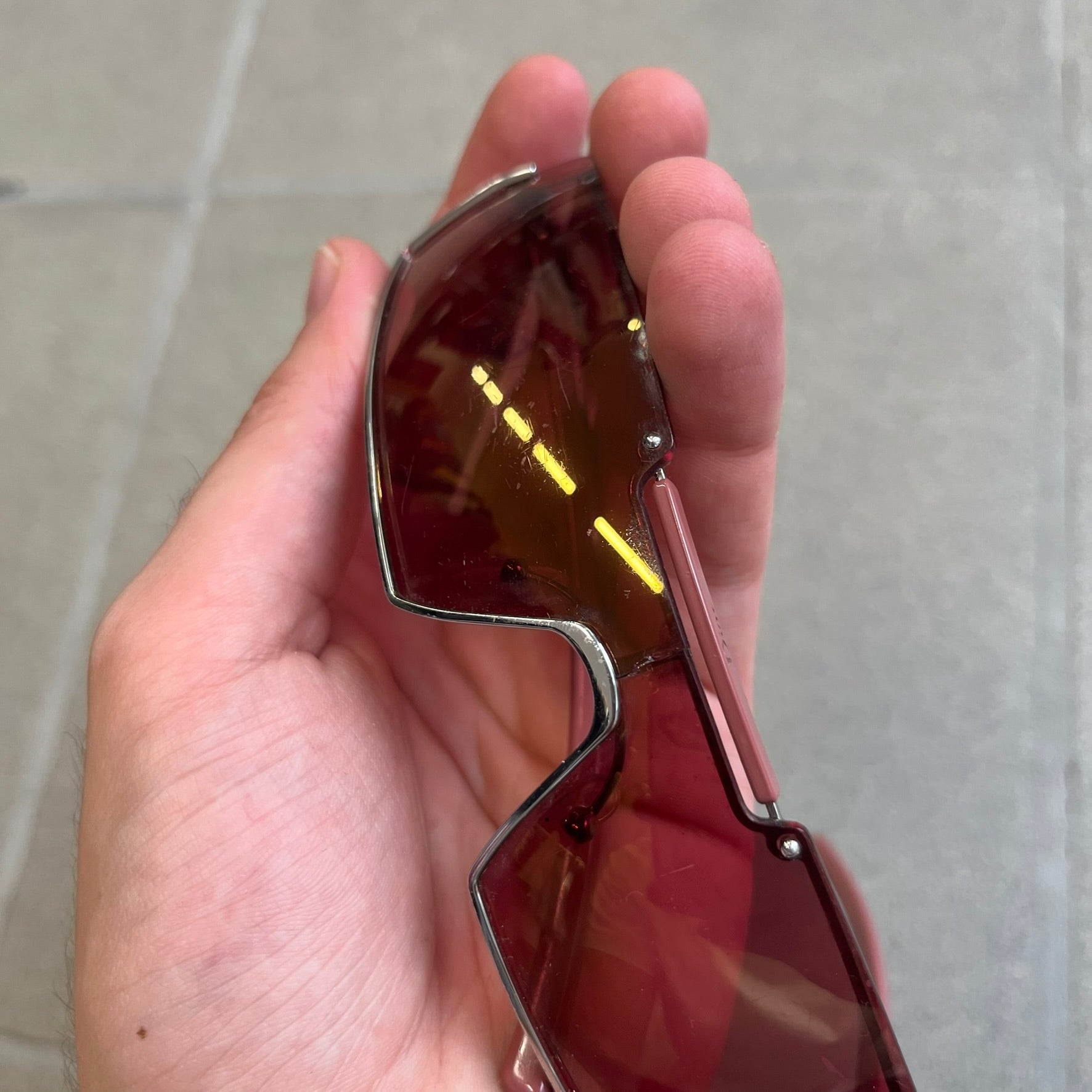 Christian Dior Viktim 2 Pink Sunglasses are an early 2000's eyewear piece from the Safilo era, featuring a futuristic rimless shield silhouette with a sleek wraparound lens design. The sunglasses have a pink/rose tinted lens with subtle Dior logo details at the bottom and minimalist framing. Made in Austria, they come complete with a silver Dior case.