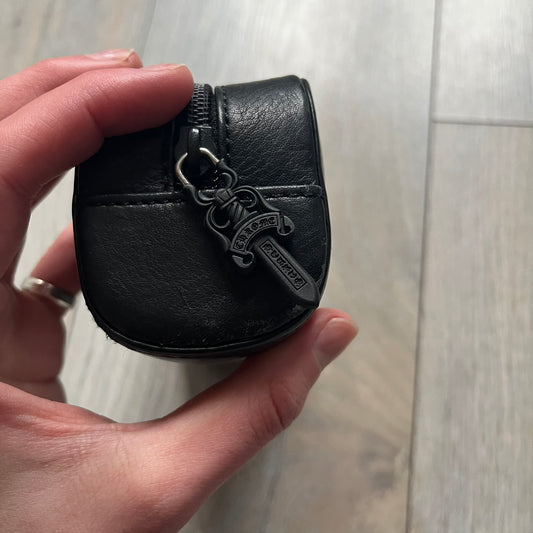 The Chrome Hearts Black Leather Sunglasses Case is a black leather zip case with a Chrome Hearts logo on the front, flanked by two cross motifs. It features a CH dagger zipper pull made from black plastic and metal. The interior is monogrammed with vine dagger logos and includes an attached soft inner compartment designed to hold a cleaning cloth.