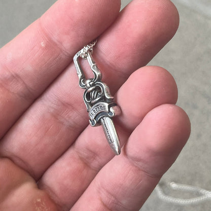 Chrome Hearts Dagger Zipper Pendant crafted from .925 silver, featuring the brand’s signature double-sided dagger design with “Chrome” on the guard and “Hearts” on the blade. Comes on a standard 925 Silver chain (non-CH). Square bail for chain attachment with 925 tag on one side and 89 03 on the other. The dagger was originally a zipper pull.
