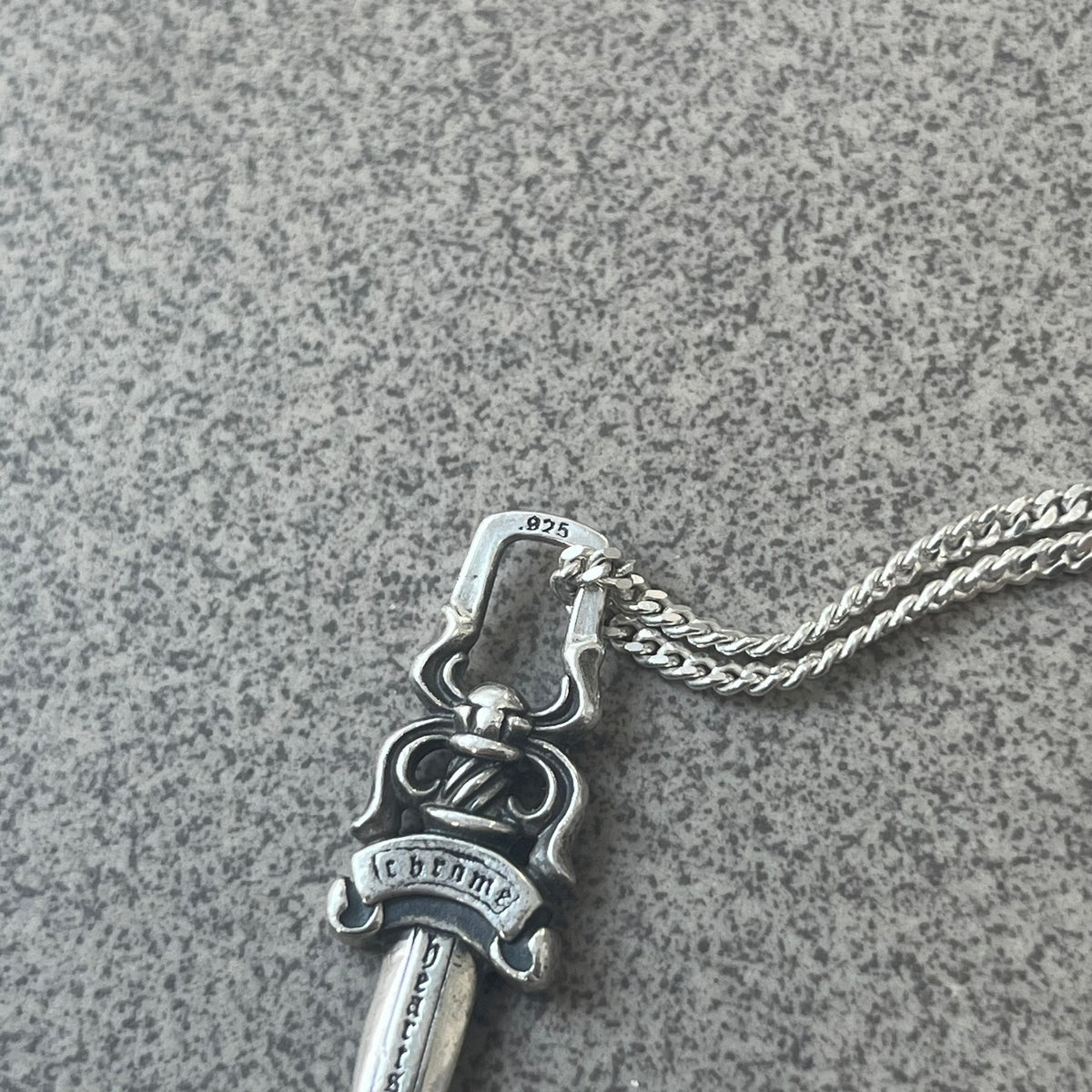Chrome Hearts Dagger Zipper Pendant crafted from .925 silver, featuring the brand’s signature double-sided dagger design with “Chrome” on the guard and “Hearts” on the blade. Comes on a standard 925 Silver chain (non-CH). Square bail for chain attachment with 925 tag on one side and 89 03 on the other. The dagger was originally a zipper pull.