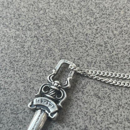 Chrome Hearts Dagger Zipper Pendant crafted from .925 silver, featuring the brand’s signature double-sided dagger design with “Chrome” on the guard and “Hearts” on the blade. Comes on a standard 925 Silver chain (non-CH). Square bail for chain attachment with 925 tag on one side and 89 03 on the other. The dagger was originally a zipper pull.
