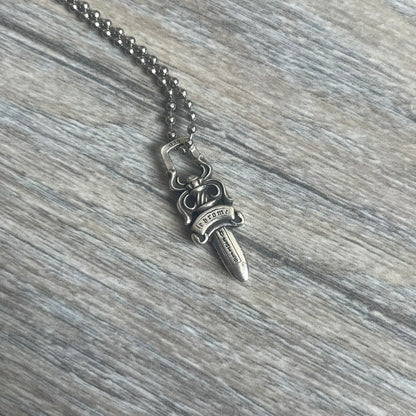Chrome Hearts Dagger Zipper Pendant crafted from .925 silver, featuring the brand’s signature double-sided dagger design with “Chrome” on the guard and “Hearts” on the blade. Comes on a standard steel ball chain (non-CH). Square bail for chain attachment with 925 tag on one side and 89 03 on the other. The dagger was originally a zipper pull.