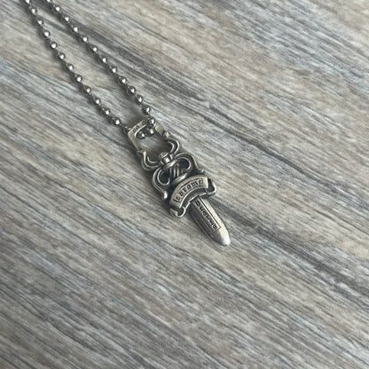 Chrome Hearts Dagger Zipper Pendant crafted from .925 silver, featuring the brand’s signature double-sided dagger design with “Chrome” on the guard and “Hearts” on the blade. Comes on a standard steel ball chain (non-CH). Square bail for chain attachment with 925 tag on one side and 89 03 on the other. The dagger was originally a zipper pull.