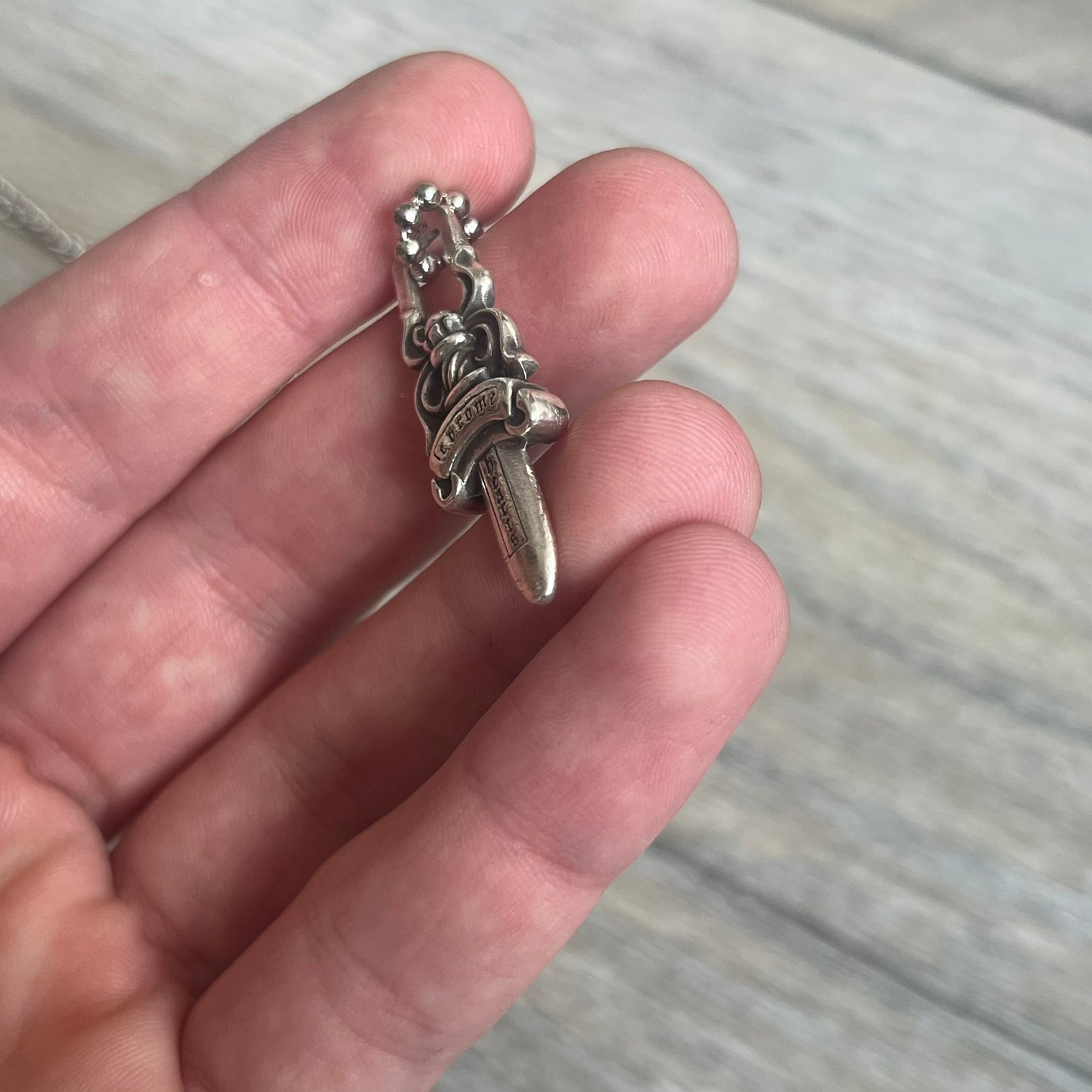 Chrome Hearts Dagger Zipper Pendant crafted from .925 silver, featuring the brand’s signature double-sided dagger design with “Chrome” on the guard and “Hearts” on the blade. Comes on a standard steel ball chain (non-CH). Square bail for chain attachment with 925 tag on one side and 89 03 on the other. The dagger was originally a zipper pull.