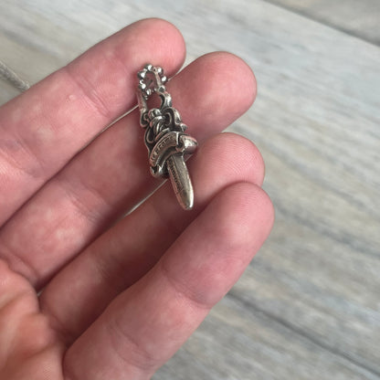 Chrome Hearts Dagger Zipper Pendant crafted from .925 silver, featuring the brand’s signature double-sided dagger design with “Chrome” on the guard and “Hearts” on the blade. Comes on a standard steel ball chain (non-CH). Square bail for chain attachment with 925 tag on one side and 89 03 on the other. The dagger was originally a zipper pull.