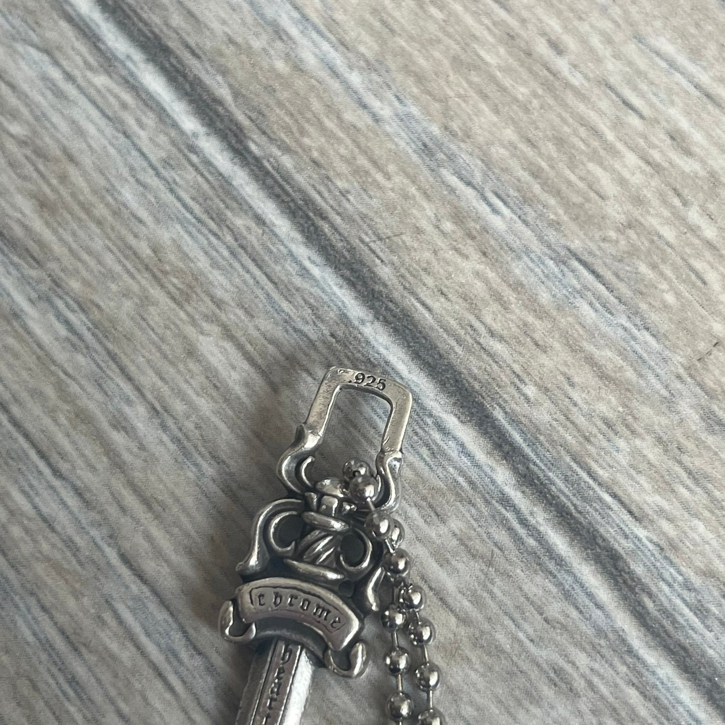 Chrome Hearts Dagger Zipper Pendant crafted from .925 silver, featuring the brand’s signature double-sided dagger design with “Chrome” on the guard and “Hearts” on the blade. Comes on a standard steel ball chain (non-CH). Square bail for chain attachment with 925 tag on one side and 89 03 on the other. The dagger was originally a zipper pull.