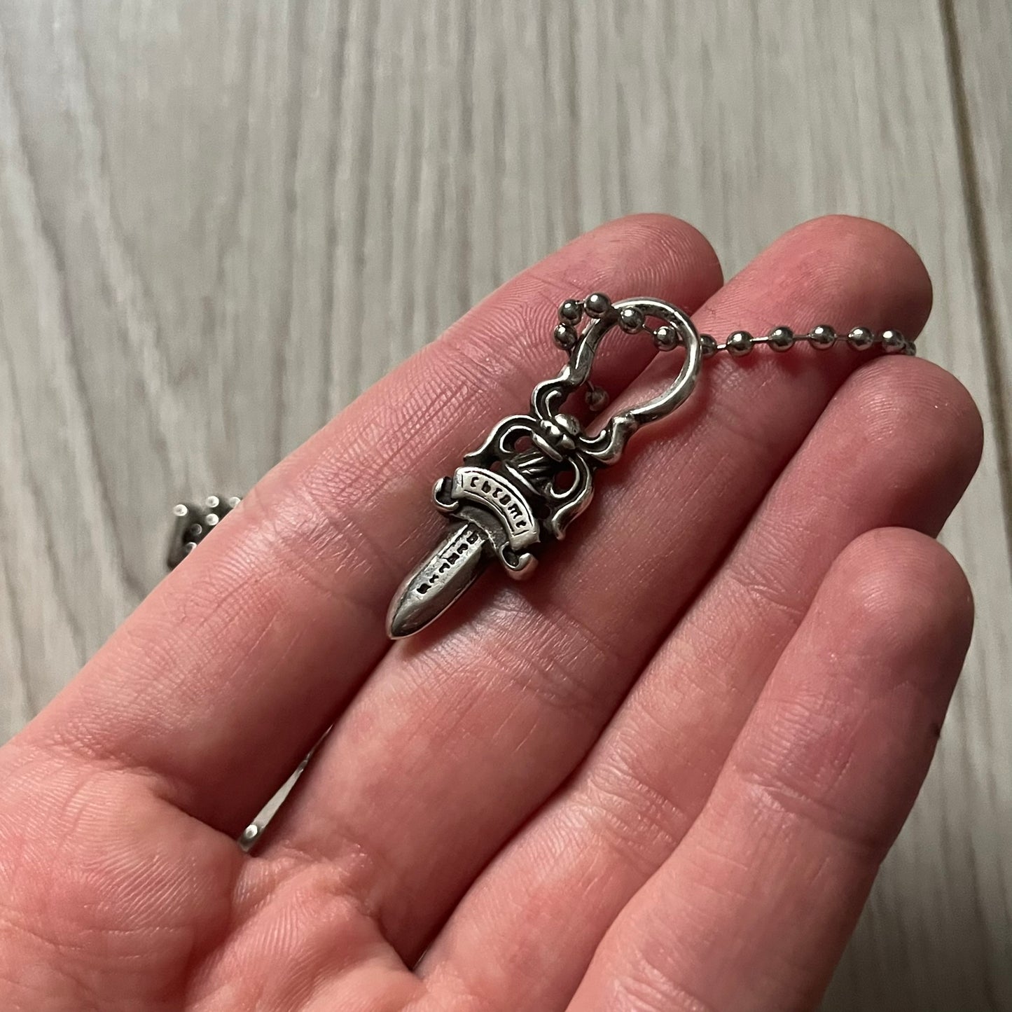 Chrome Hearts Dagger Zipper Pendant crafted from .925 silver, featuring the brand’s signature double-sided dagger design with “Chrome” on the guard and “Hearts” on the blade. Comes on a standard steel ball chain (non-CH). Circular bail for chain attachment. The dagger was originally a zipper pull.