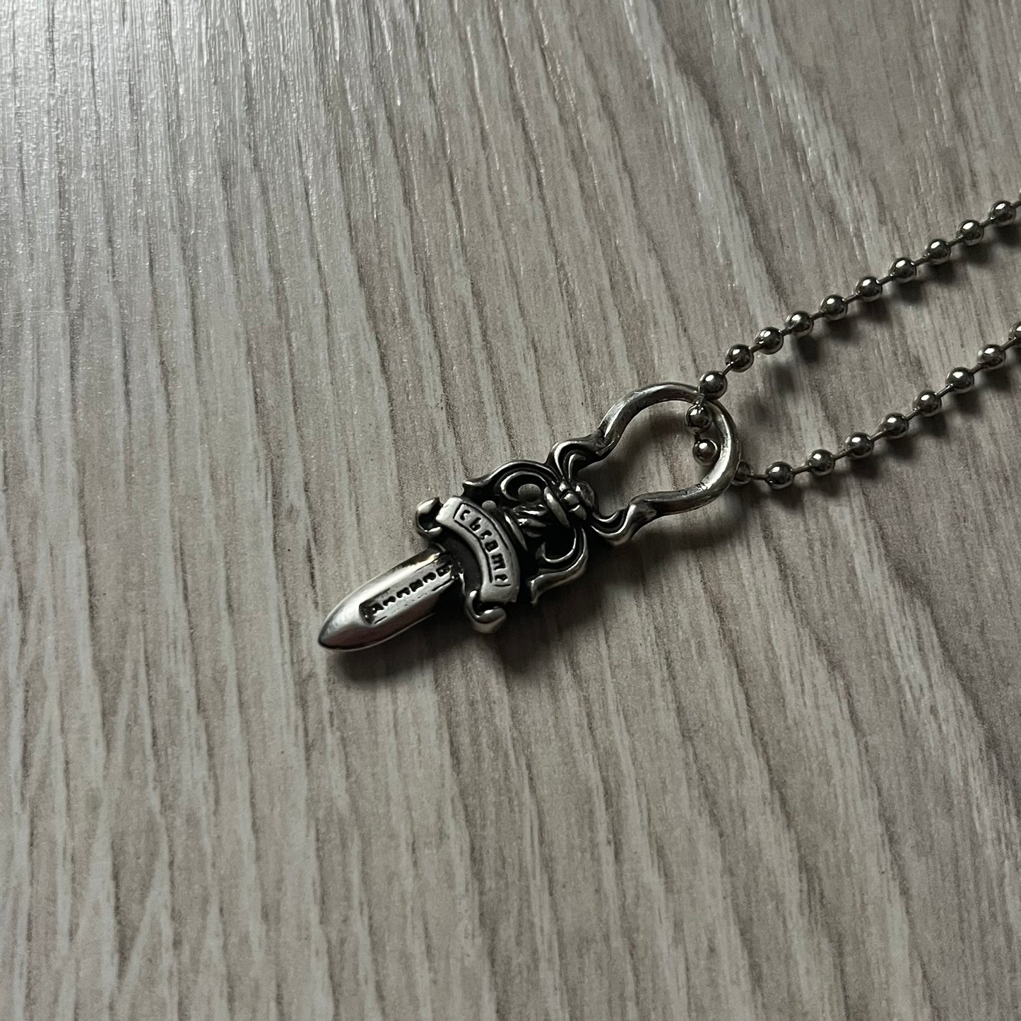 Chrome Hearts Dagger Zipper Pendant crafted from .925 silver, featuring the brand’s signature double-sided dagger design with “Chrome” on the guard and “Hearts” on the blade. Comes on a standard steel ball chain (non-CH). Circular bail for chain attachment. The dagger was originally a zipper pull.