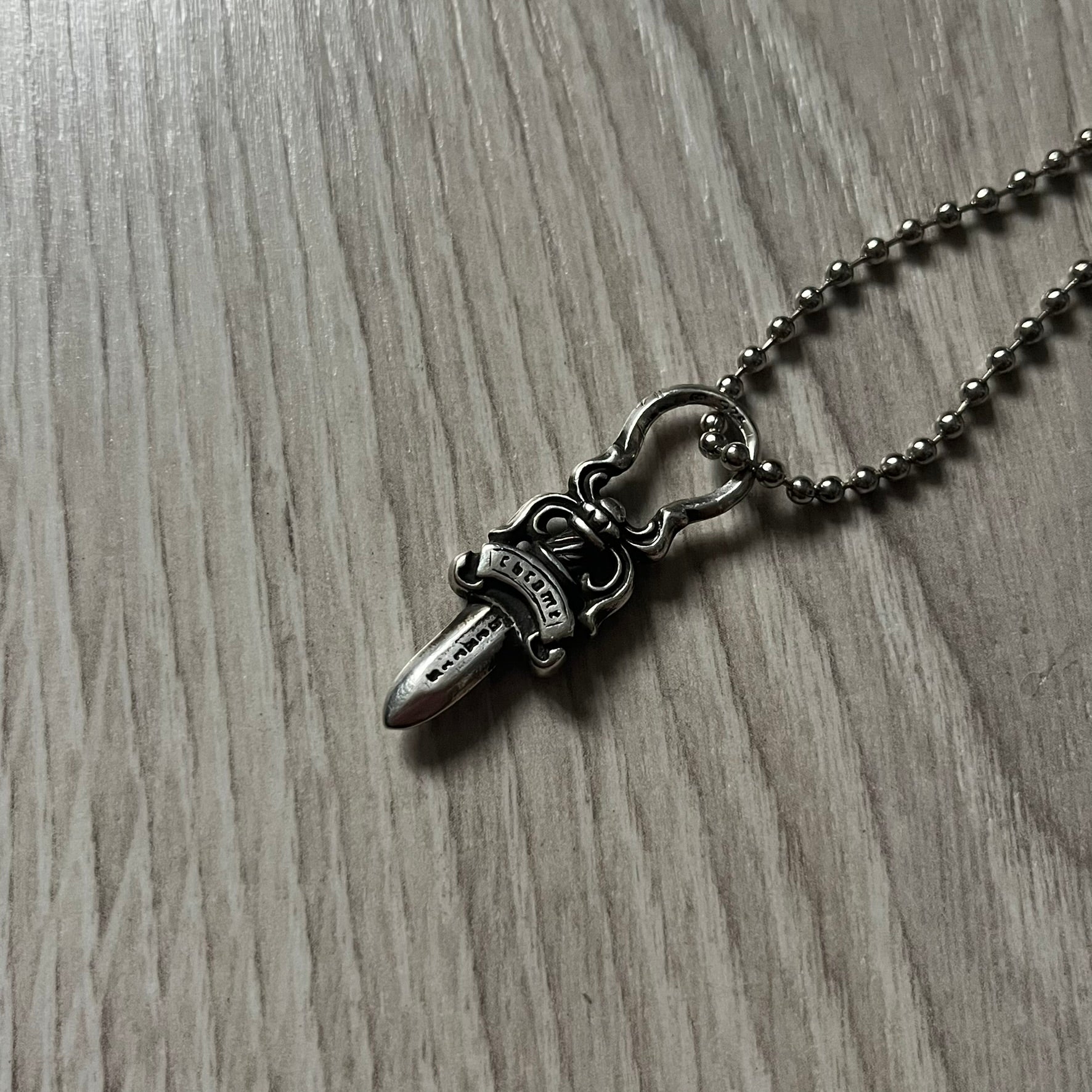 Chrome Hearts Dagger Zipper Pendant crafted from .925 silver, featuring the brand’s signature double-sided dagger design with “Chrome” on the guard and “Hearts” on the blade. Comes on a standard steel ball chain (non-CH). Circular bail for chain attachment. The dagger was originally a zipper pull.