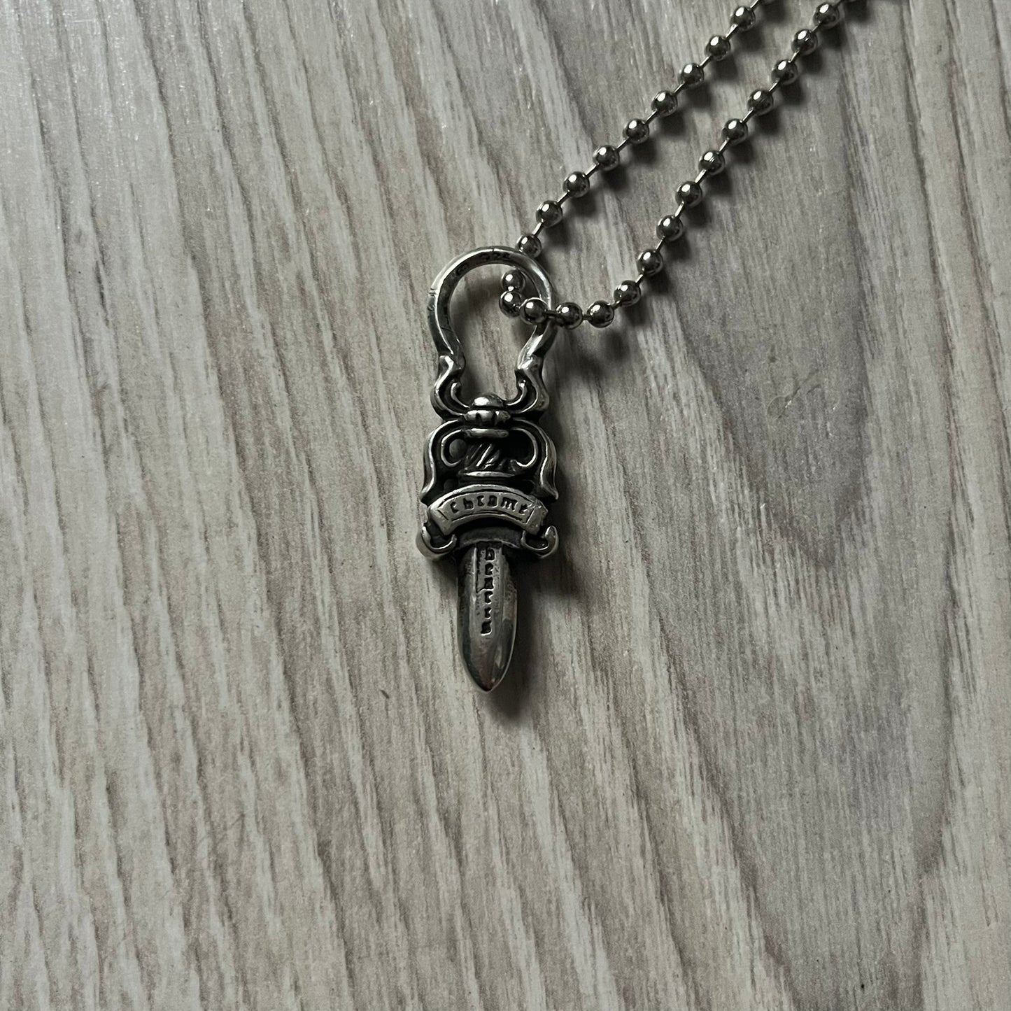 Chrome Hearts Dagger Zipper Pendant crafted from .925 silver, featuring the brand’s signature double-sided dagger design with “Chrome” on the guard and “Hearts” on the blade. Comes on a standard steel ball chain (non-CH). Circular bail for chain attachment. The dagger was originally a zipper pull.