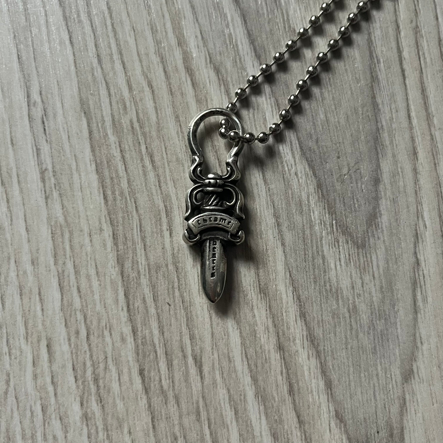 Chrome Hearts Dagger Zipper Pendant crafted from .925 silver, featuring the brand’s signature double-sided dagger design with “Chrome” on the guard and “Hearts” on the blade. Comes on a standard steel ball chain (non-CH). Circular bail for chain attachment. The dagger was originally a zipper pull.