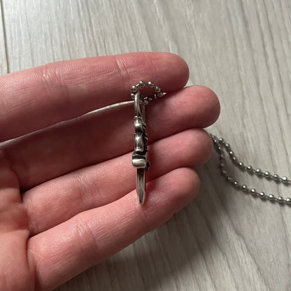 Chrome Hearts Dagger Zipper Pendant crafted from .925 silver, featuring the brand’s signature double-sided dagger design with “Chrome” on the guard and “Hearts” on the blade. Comes on a standard steel ball chain (non-CH). Circular bail for chain attachment. The dagger was originally a zipper pull.