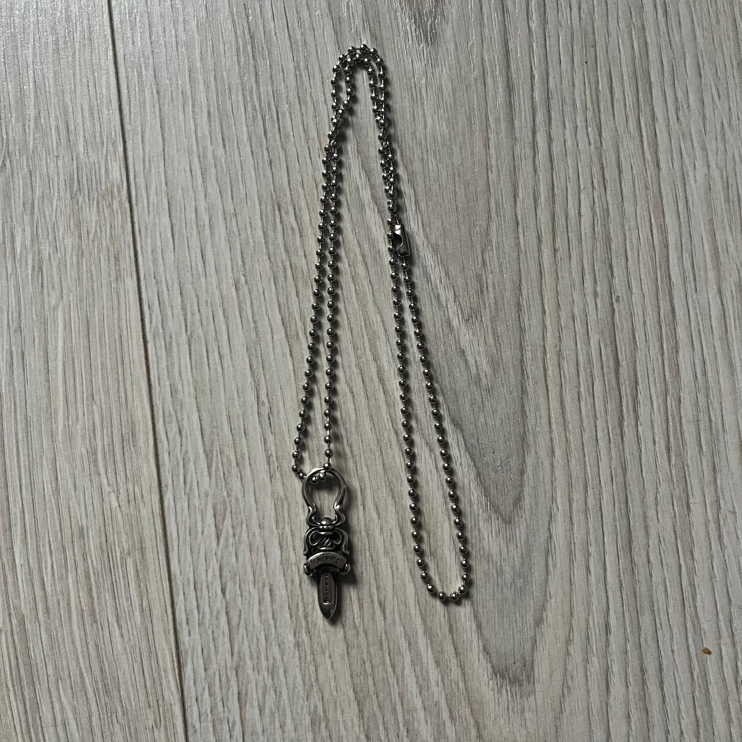 Chrome Hearts Dagger Zipper Pendant crafted from .925 silver, featuring the brand’s signature double-sided dagger design with “Chrome” on the guard and “Hearts” on the blade. Comes on a standard steel ball chain (non-CH). Circular bail for chain attachment. The dagger was originally a zipper pull.