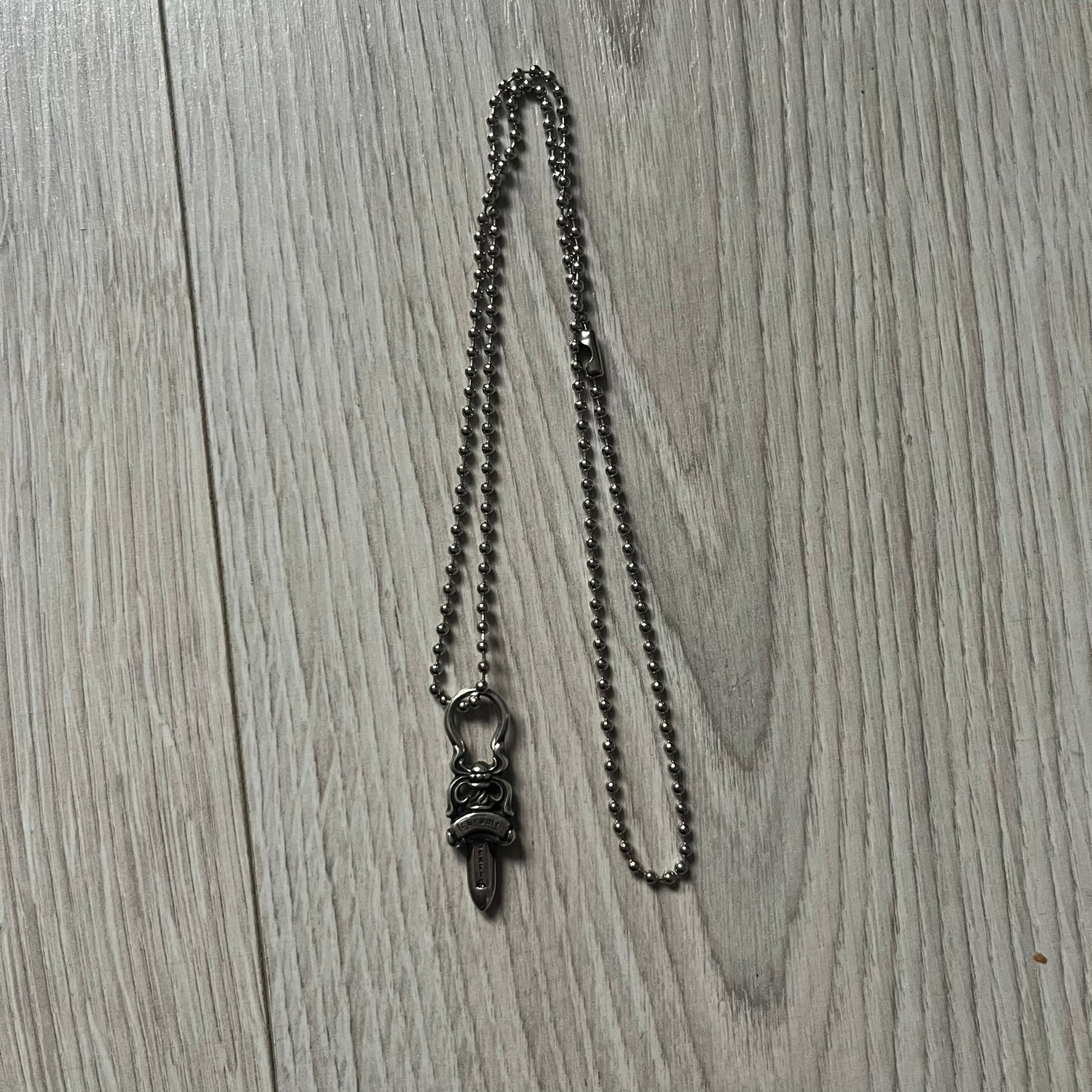 Chrome Hearts Dagger Zipper Pendant crafted from .925 silver, featuring the brand’s signature double-sided dagger design with “Chrome” on the guard and “Hearts” on the blade. Comes on a standard steel ball chain (non-CH). Circular bail for chain attachment. The dagger was originally a zipper pull.