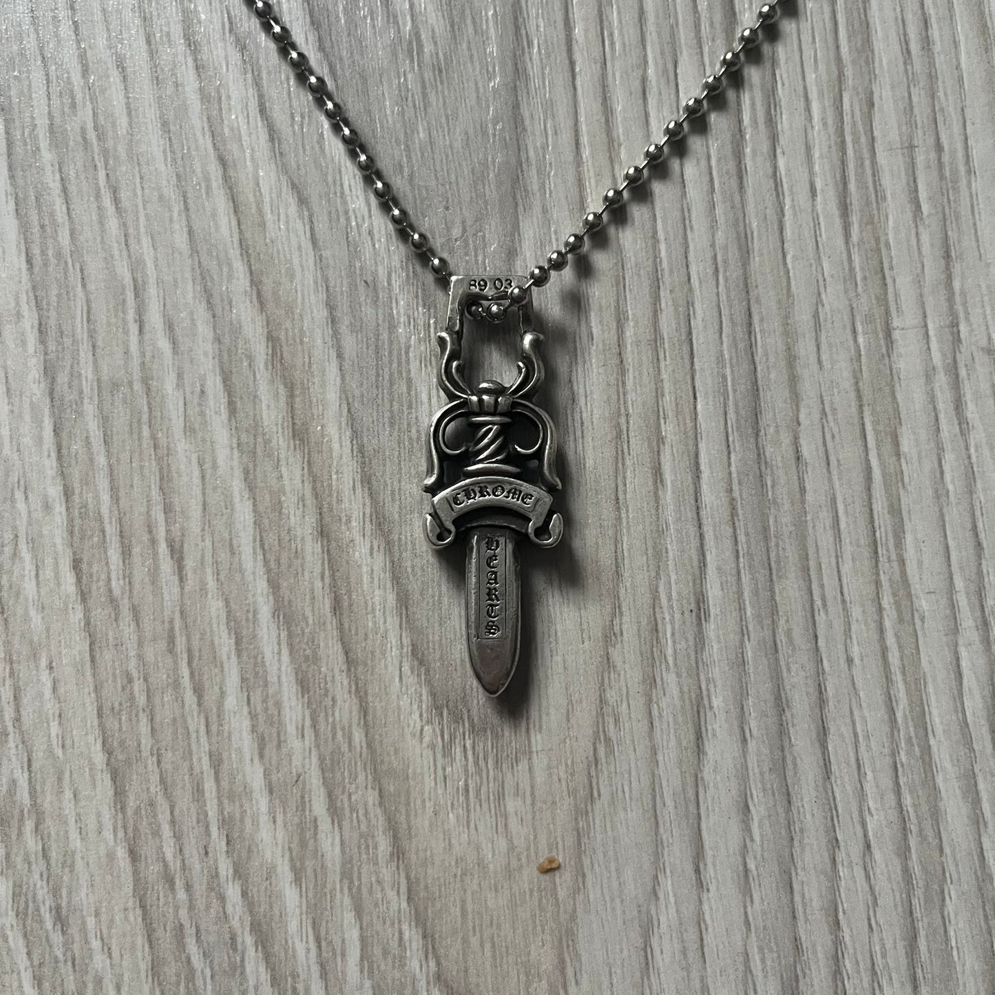 Chrome Hearts Dagger #10 Pendant crafted from genuine .925 silver, featuring the brand’s signature double-sided dagger design with “Chrome” on the guard and “Hearts” on the blade. Comes on a standard steel ball chain (non-CH). The top rectangular bail includes engraved markings: “89/03” on one side and “Sterling” on the other.&nbsp;