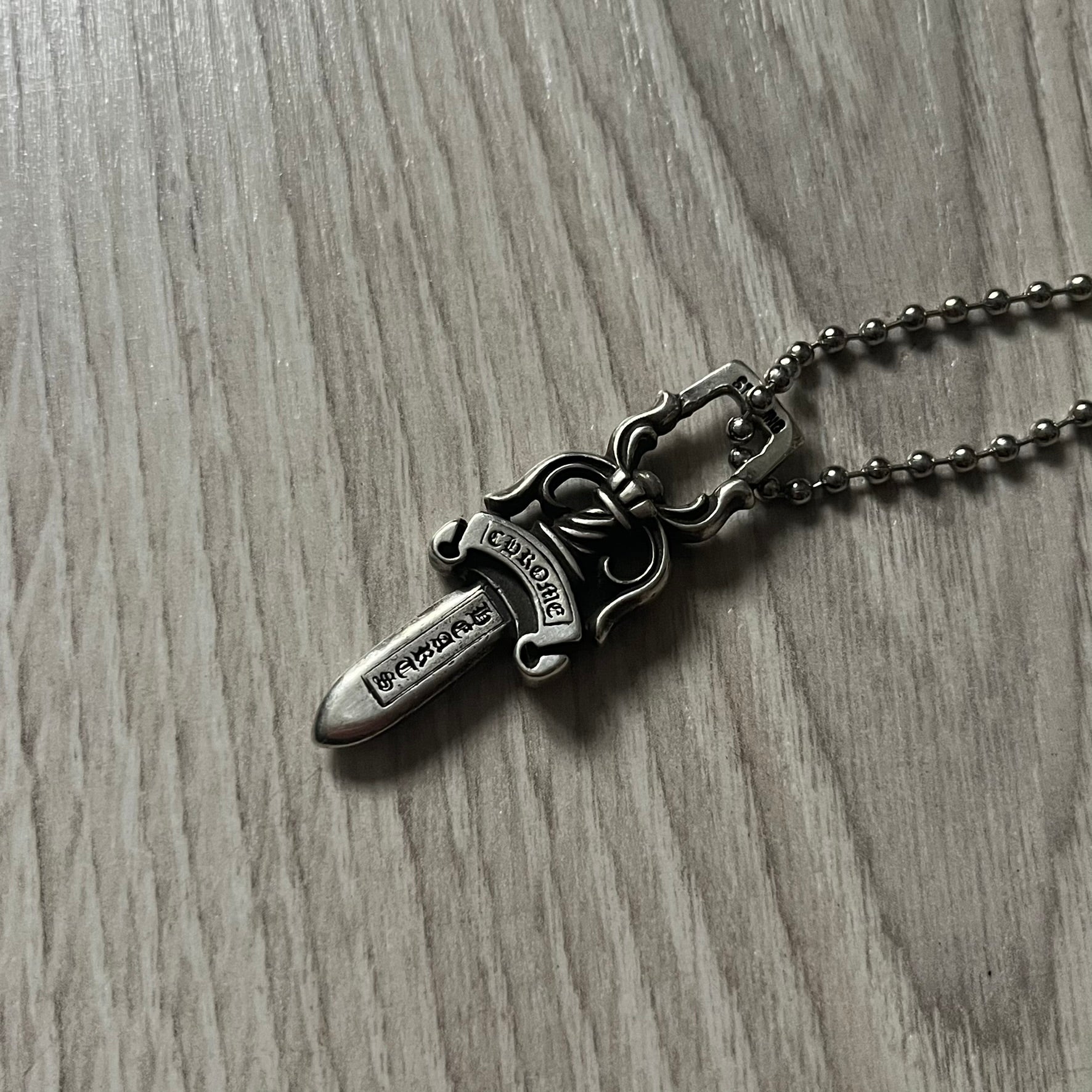 Chrome Hearts Dagger #10 Pendant crafted from genuine .925 silver, featuring the brand’s signature double-sided dagger design with “Chrome” on the guard and “Hearts” on the blade. Comes on a standard steel ball chain (non-CH). The top rectangular bail includes engraved markings: “89/03” on one side and “Sterling” on the other.&nbsp;