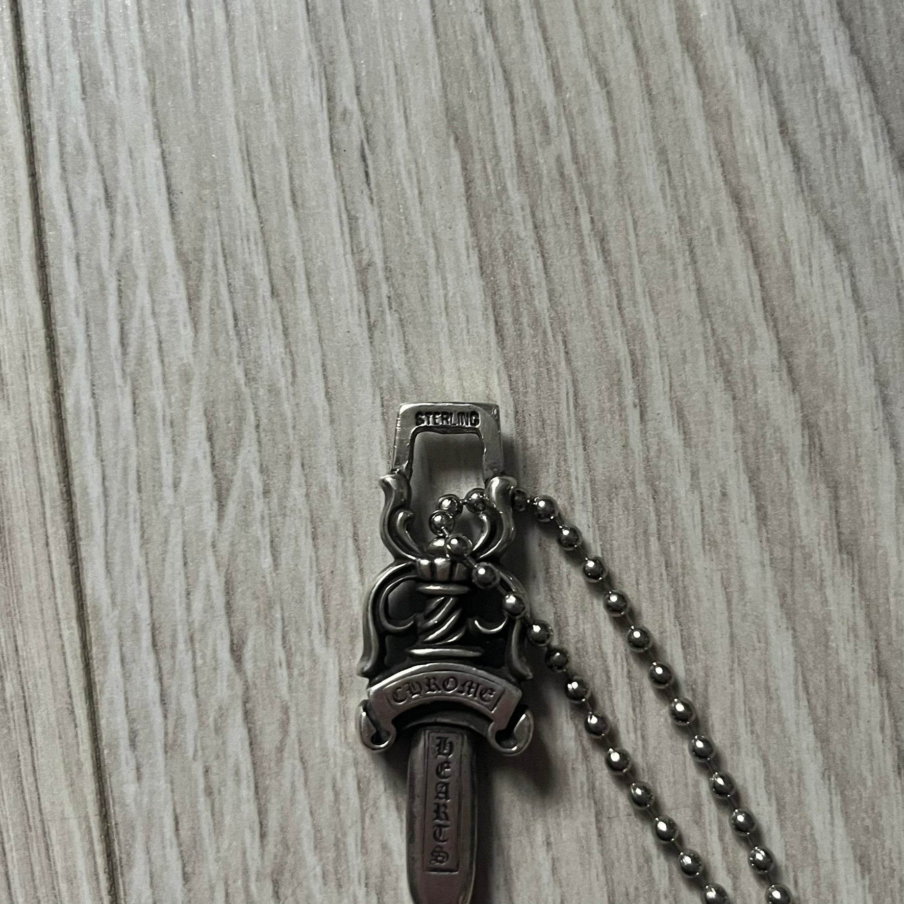 Chrome Hearts Dagger #10 Pendant crafted from genuine .925 silver, featuring the brand’s signature double-sided dagger design with “Chrome” on the guard and “Hearts” on the blade. Comes on a standard steel ball chain (non-CH). The top rectangular bail includes engraved markings: “89/03” on one side and “Sterling” on the other.&nbsp;