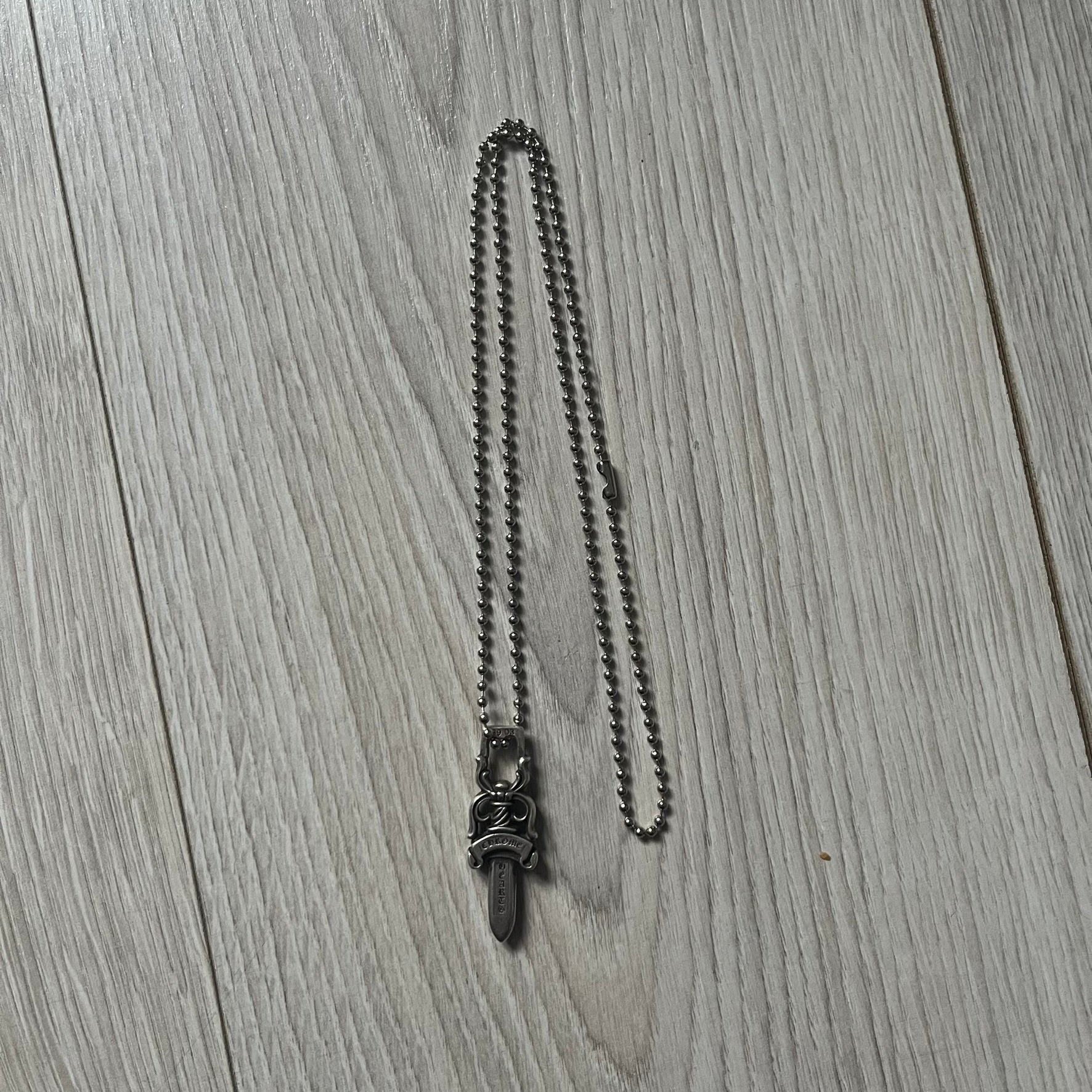 Chrome Hearts Dagger #10 Pendant crafted from genuine .925 silver, featuring the brand’s signature double-sided dagger design with “Chrome” on the guard and “Hearts” on the blade. Comes on a standard steel ball chain (non-CH). The top rectangular bail includes engraved markings: “89/03” on one side and “Sterling” on the other.&nbsp;