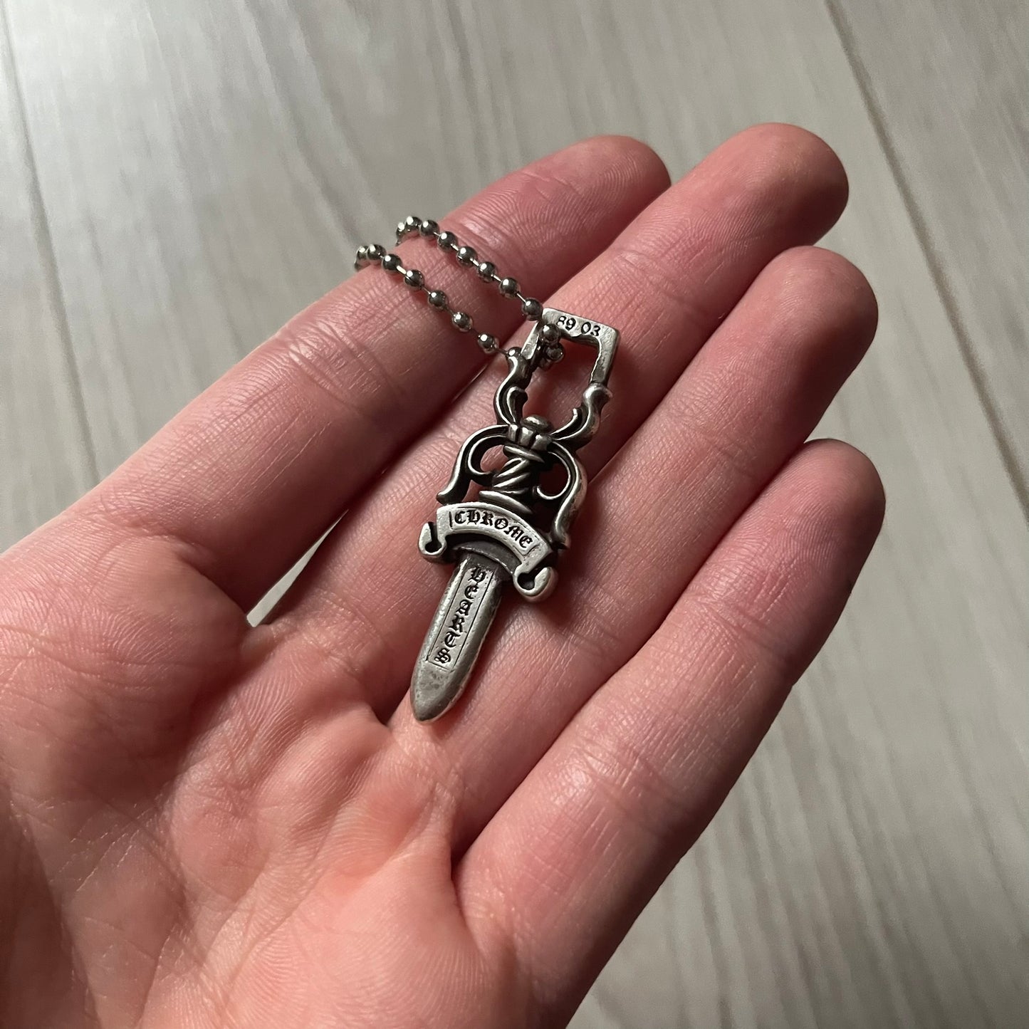 Chrome Hearts Dagger #10 Pendant crafted from genuine .925 silver, featuring the brand’s signature double-sided dagger design with “Chrome” on the guard and “Hearts” on the blade. Comes on a standard steel ball chain (non-CH). The top rectangular bail includes engraved markings: “89/03” on one side and “Sterling” on the other.&nbsp;