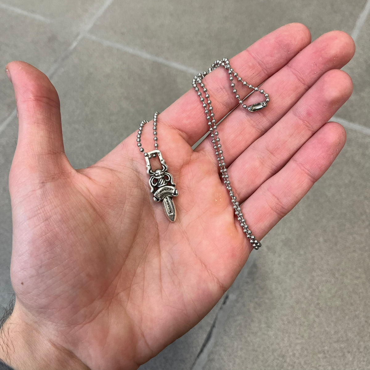 Chrome Hearts #5 Keychain Dagger Necklace crafted from .925 silver, featuring the brand’s signature double-sided dagger design with “Chrome” on the guard and “Hearts” on the blade. Comes on a stainless steel ball chain (non-CH). Square bail for chain attachment, the dagger was originally a keychain.