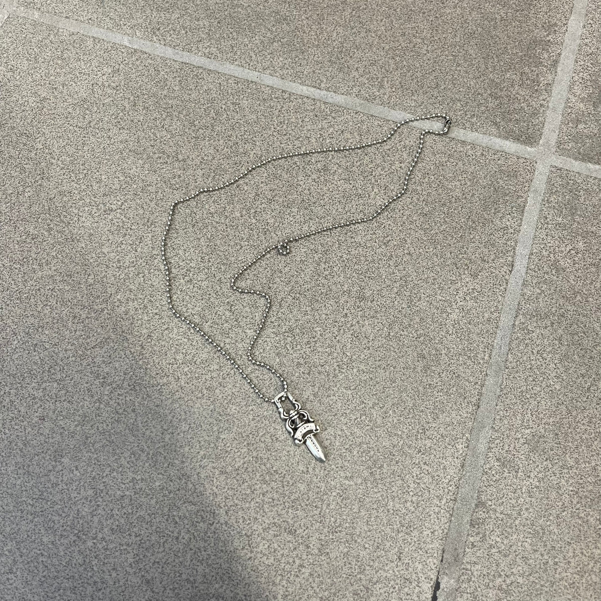 Chrome Hearts #5 Keychain Dagger Necklace crafted from .925 silver, featuring the brand’s signature double-sided dagger design with “Chrome” on the guard and “Hearts” on the blade. Comes on a stainless steel ball chain (non-CH). Square bail for chain attachment, the dagger was originally a keychain.