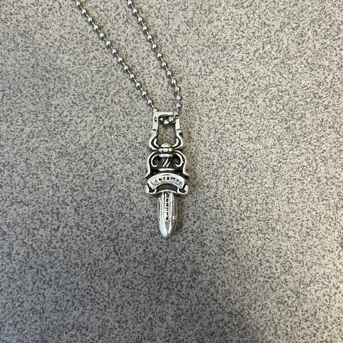 Chrome Hearts #5 Keychain Dagger Necklace crafted from .925 silver, featuring the brand’s signature double-sided dagger design with “Chrome” on the guard and “Hearts” on the blade. Comes on a stainless steel ball chain (non-CH). Square bail for chain attachment, the dagger was originally a keychain.