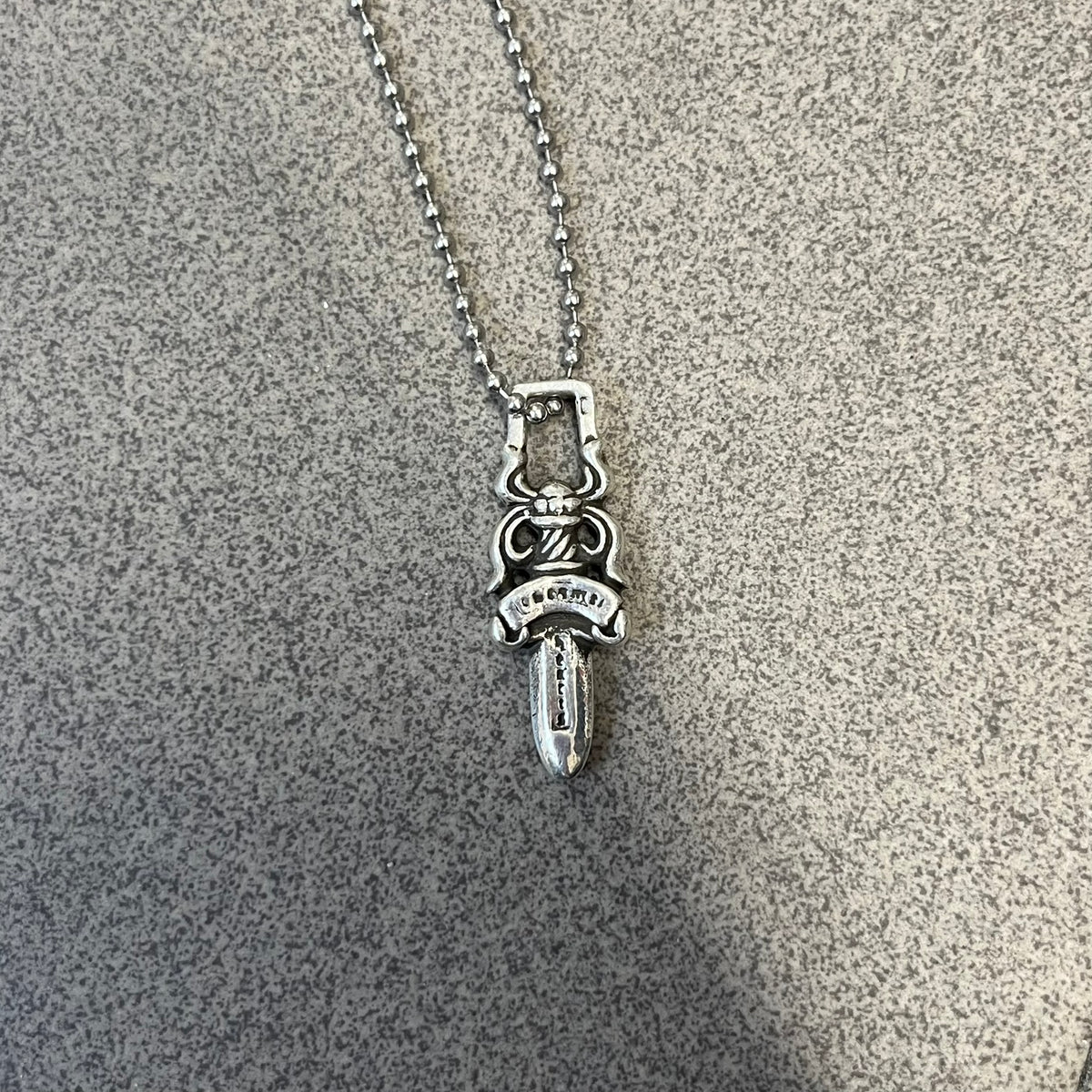 Chrome Hearts #5 Keychain Dagger Necklace crafted from .925 silver, featuring the brand’s signature double-sided dagger design with “Chrome” on the guard and “Hearts” on the blade. Comes on a stainless steel ball chain (non-CH). Square bail for chain attachment, the dagger was originally a keychain.