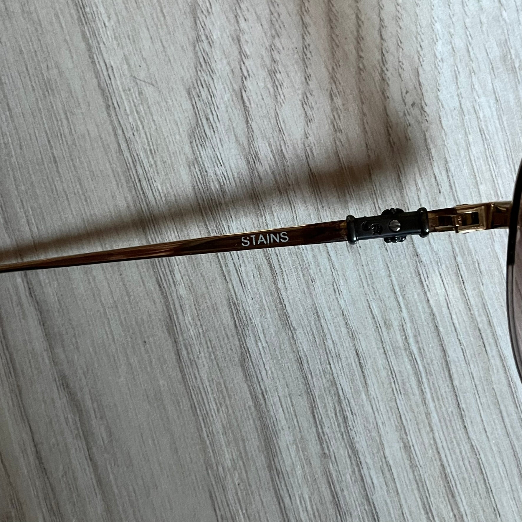 Chrome Hearts Stains Gold Sunglasses featuring a gold-tone metal frame with brown mirror-coated plastic lenses. Made in Japan, this model includes aged silver Chrome Hearts cross detailing wrapped around the arms, cut-out cross accents at the arm tips, and visible Chrome Hearts branding on the bridge and top of the frame. Additional cross branding appears on the nose pads. Comes complete with the original black leather Chrome Hearts zip case, finished with exterior branding and a dagger-shaped zipper pull.