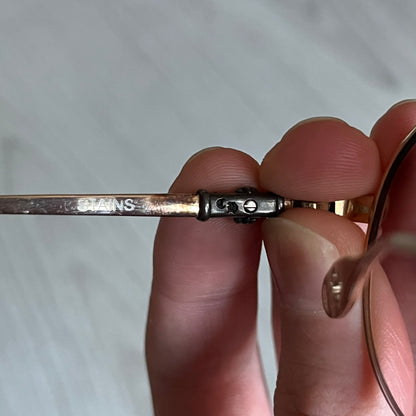 Chrome Hearts Stains Gold Sunglasses featuring a gold-tone metal frame with brown mirror-coated plastic lenses. Made in Japan, this model includes aged silver Chrome Hearts cross detailing wrapped around the arms, cut-out cross accents at the arm tips, and visible Chrome Hearts branding on the bridge and top of the frame. Additional cross branding appears on the nose pads. Comes complete with the original black leather Chrome Hearts zip case, finished with exterior branding and a dagger-shaped zipper pull.