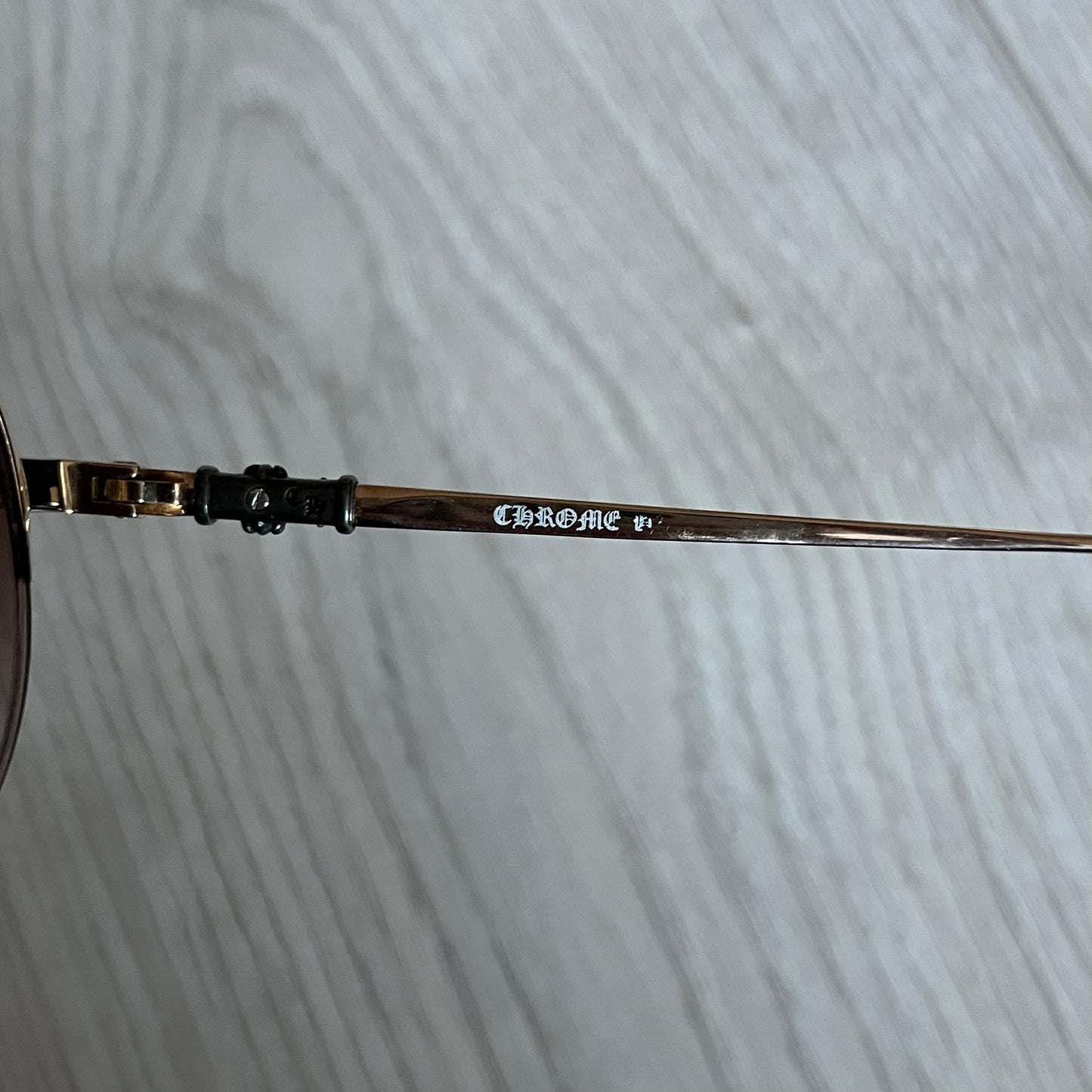 Chrome Hearts Stains Gold Sunglasses featuring a gold-tone metal frame with brown mirror-coated plastic lenses. Made in Japan, this model includes aged silver Chrome Hearts cross detailing wrapped around the arms, cut-out cross accents at the arm tips, and visible Chrome Hearts branding on the bridge and top of the frame. Additional cross branding appears on the nose pads. Comes complete with the original black leather Chrome Hearts zip case, finished with exterior branding and a dagger-shaped zipper pull.