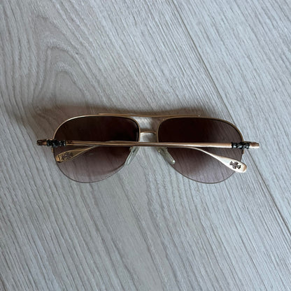 Chrome Hearts Stains Gold Sunglasses featuring a gold-tone metal frame with brown mirror-coated plastic lenses. Made in Japan, this model includes aged silver Chrome Hearts cross detailing wrapped around the arms, cut-out cross accents at the arm tips, and visible Chrome Hearts branding on the bridge and top of the frame. Additional cross branding appears on the nose pads. Comes complete with the original black leather Chrome Hearts zip case, finished with exterior branding and a dagger-shaped zipper pull.