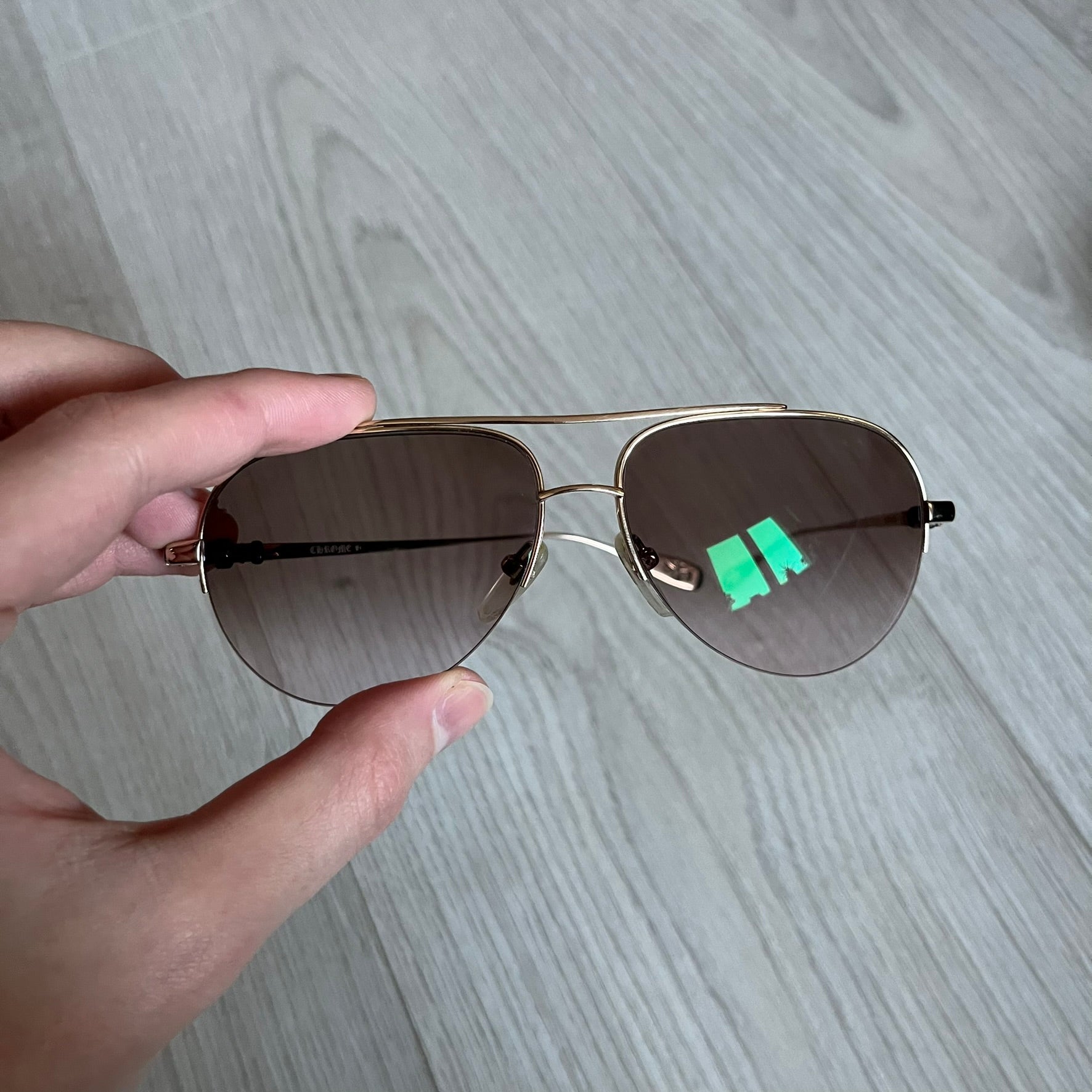 Chrome Hearts Stains Gold Sunglasses featuring a gold-tone metal frame with brown mirror-coated plastic lenses. Made in Japan, this model includes aged silver Chrome Hearts cross detailing wrapped around the arms, cut-out cross accents at the arm tips, and visible Chrome Hearts branding on the bridge and top of the frame. Additional cross branding appears on the nose pads. Comes complete with the original black leather Chrome Hearts zip case, finished with exterior branding and a dagger-shaped zipper pull.