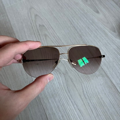 Chrome Hearts Stains Gold Sunglasses featuring a gold-tone metal frame with brown mirror-coated plastic lenses. Made in Japan, this model includes aged silver Chrome Hearts cross detailing wrapped around the arms, cut-out cross accents at the arm tips, and visible Chrome Hearts branding on the bridge and top of the frame. Additional cross branding appears on the nose pads. Comes complete with the original black leather Chrome Hearts zip case, finished with exterior branding and a dagger-shaped zipper pull.