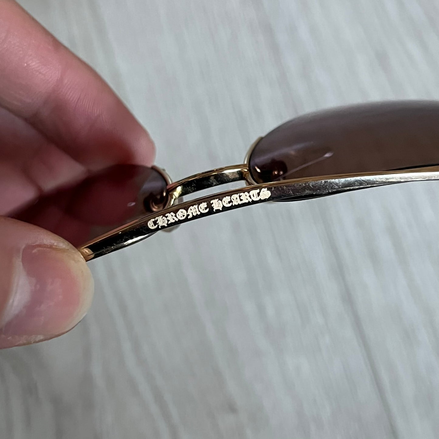 Chrome Hearts Stains Gold Sunglasses featuring a gold-tone metal frame with brown mirror-coated plastic lenses. Made in Japan, this model includes aged silver Chrome Hearts cross detailing wrapped around the arms, cut-out cross accents at the arm tips, and visible Chrome Hearts branding on the bridge and top of the frame. Additional cross branding appears on the nose pads. Comes complete with the original black leather Chrome Hearts zip case, finished with exterior branding and a dagger-shaped zipper pull.