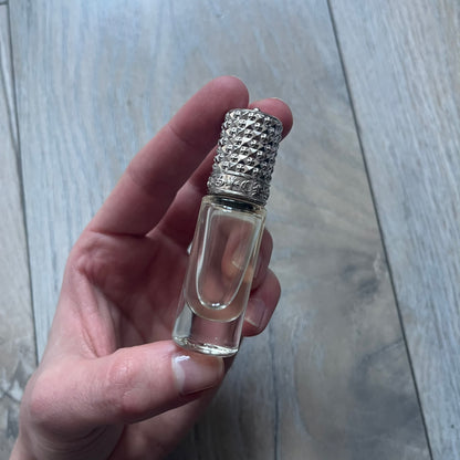 Chrome Hearts +22+ Roll-On Perfume features an aromatic oil blend with prominent jasmine and bergamot notes, designed as a concentrated roll-on fragrance. It is housed in a crystal bottle with a rhodium-plated sterling silver closure, hand crafted in France. The silver cap is detailed with raised Chrome Hearts crosses throughout, a larger cross on top, and embossed Chrome Hearts text wrapping around the base of the closure.